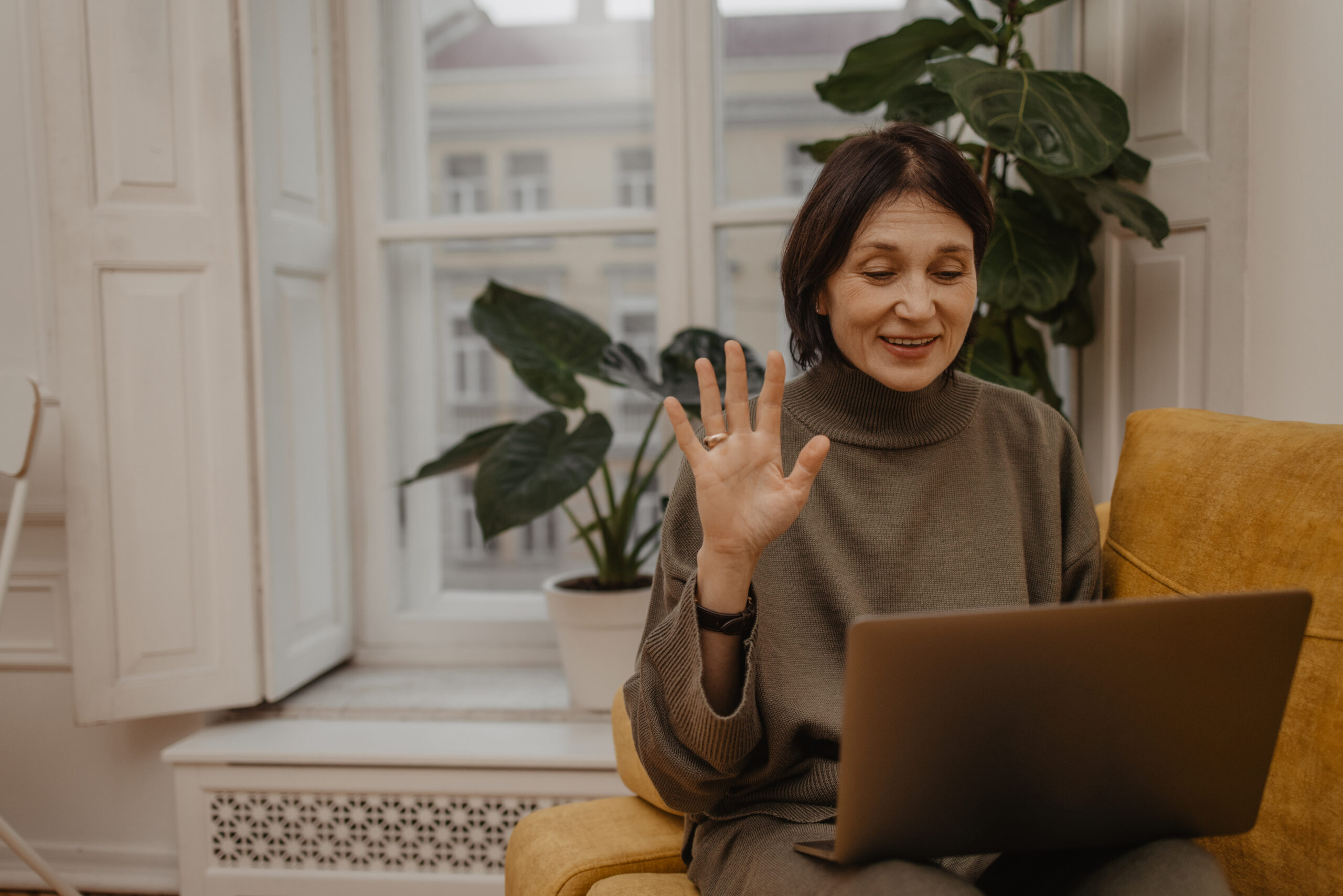 Happy middle aged caucasian woman on sofa and holding laptop while having video call with family.